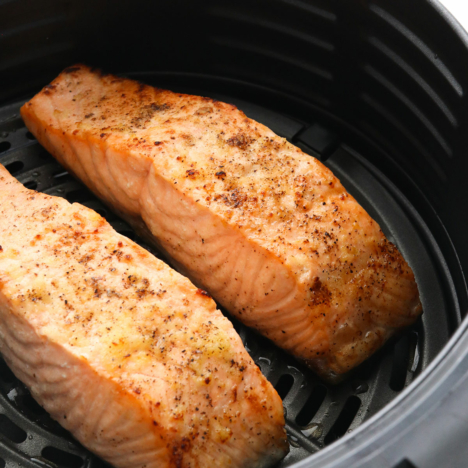 two salmon fillets cooked in a black air fryer basket.