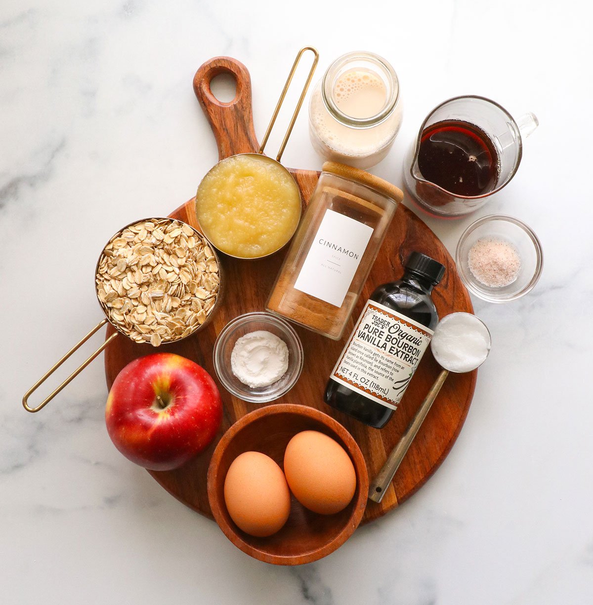 oats, applesauce, cinnamon, eggs, vanilla, and milk on a cutting board.