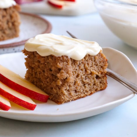 applesauce cake slice topped with cream cheese frosting on a white plate.