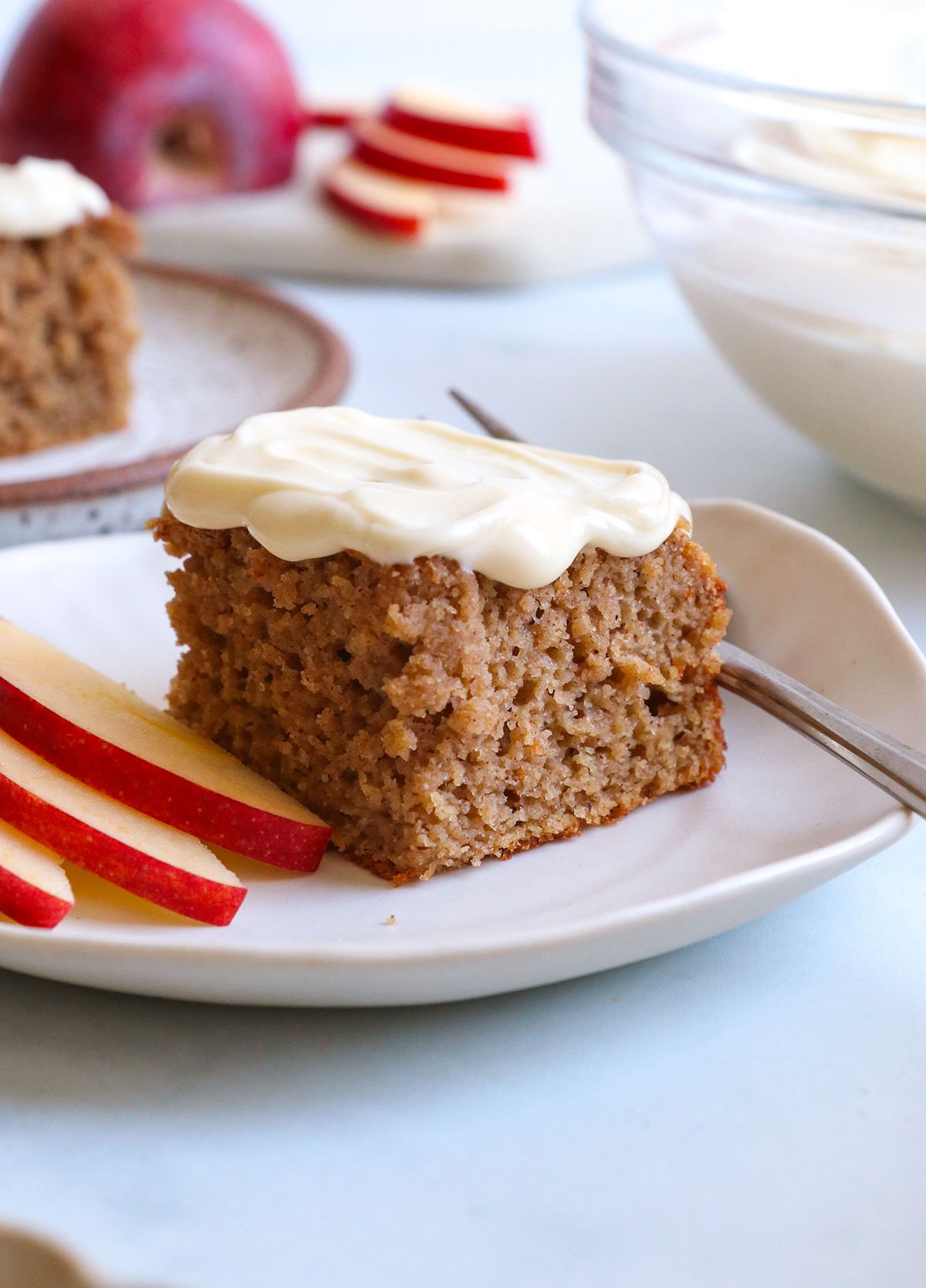 applesauce cake slice topped with cream cheese frosting on a white plate.