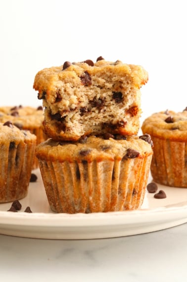 almond flour banana muffins stacked on a plate with bite taken out of it.