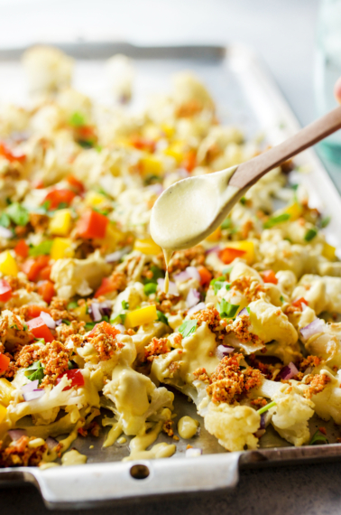 spoon drizzling sauce on vegan cauliflower nachos