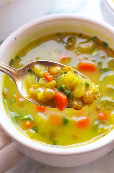 detox soup lifted up on a spoon from a white mug.