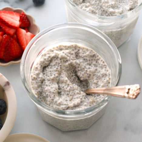 protein chia pudding in two jars near bowls of fresh berries.