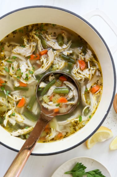 chicken vegetable soup in white pot with ladle.