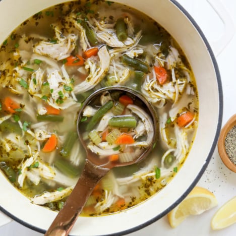 chicken vegetable soup in white pot with ladle.