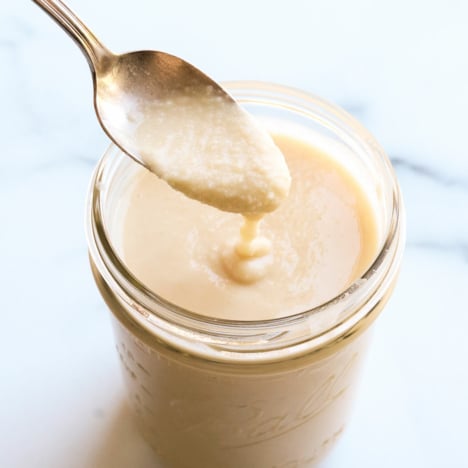 homemade coconut butter dripping off of a spoon into a jar.