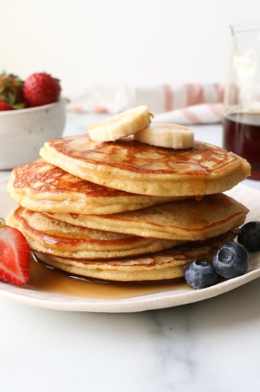 coconut flour pancakes stacked on a plate with fruit.