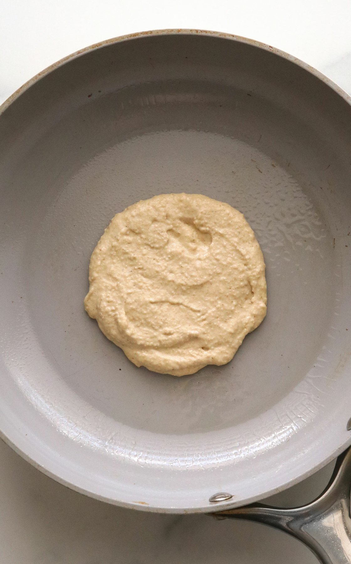 thick pancake batter spread into a circle on a gray pan.