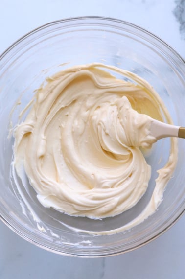 cream cheese frosting in a glass bowl stirred with a white spatula.