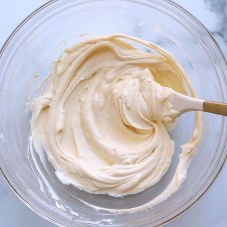 cream cheese frosting in a glass bowl stirred with a white spatula.