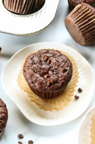 Chocolate zucchini muffin served on a white plate with the wrapper peeled off.