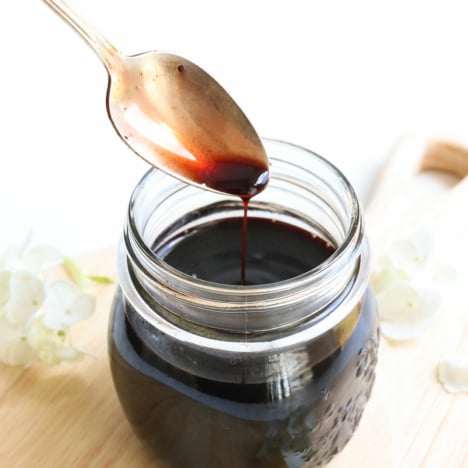 homemade elderberry syrup dripping off a spoon into a jar.