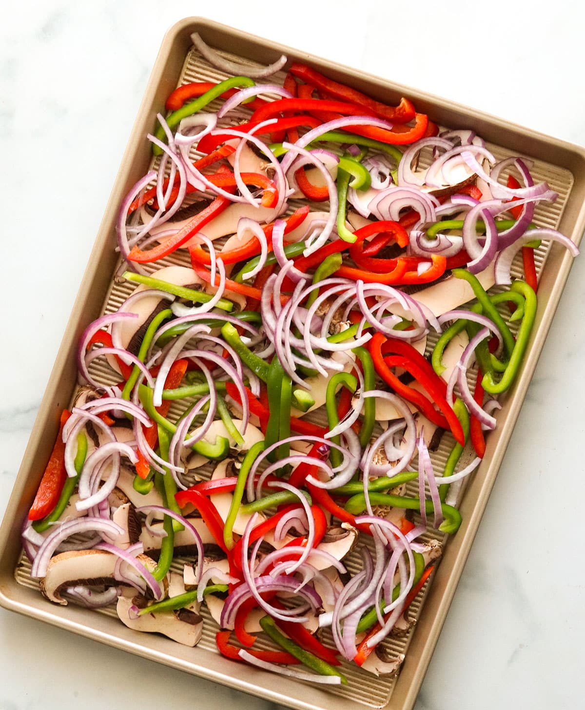 sliced fajita veggies on a half sheet pan.