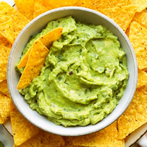 Closeup of the best guacamole served in a bowl with yellow corn chips.