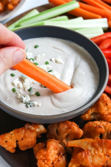 carrot dipped into a bowl of healthy blue cheese dressing.