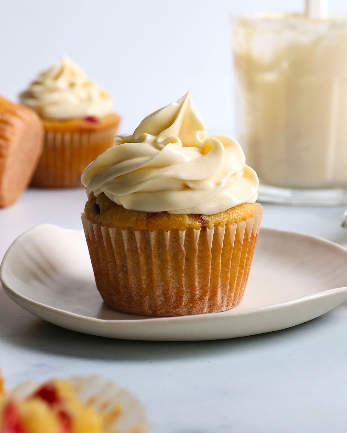 healthy cream cheese frosting piped on top of a muffin on a white plate.