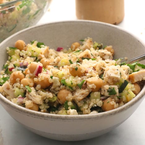 quinoa salad with chickpeas, red onion, and chicken in a bowl with fresh herbs.