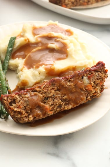 vegan meatloaf slice on a plate with mashed potatoes, green beans, and gravy.