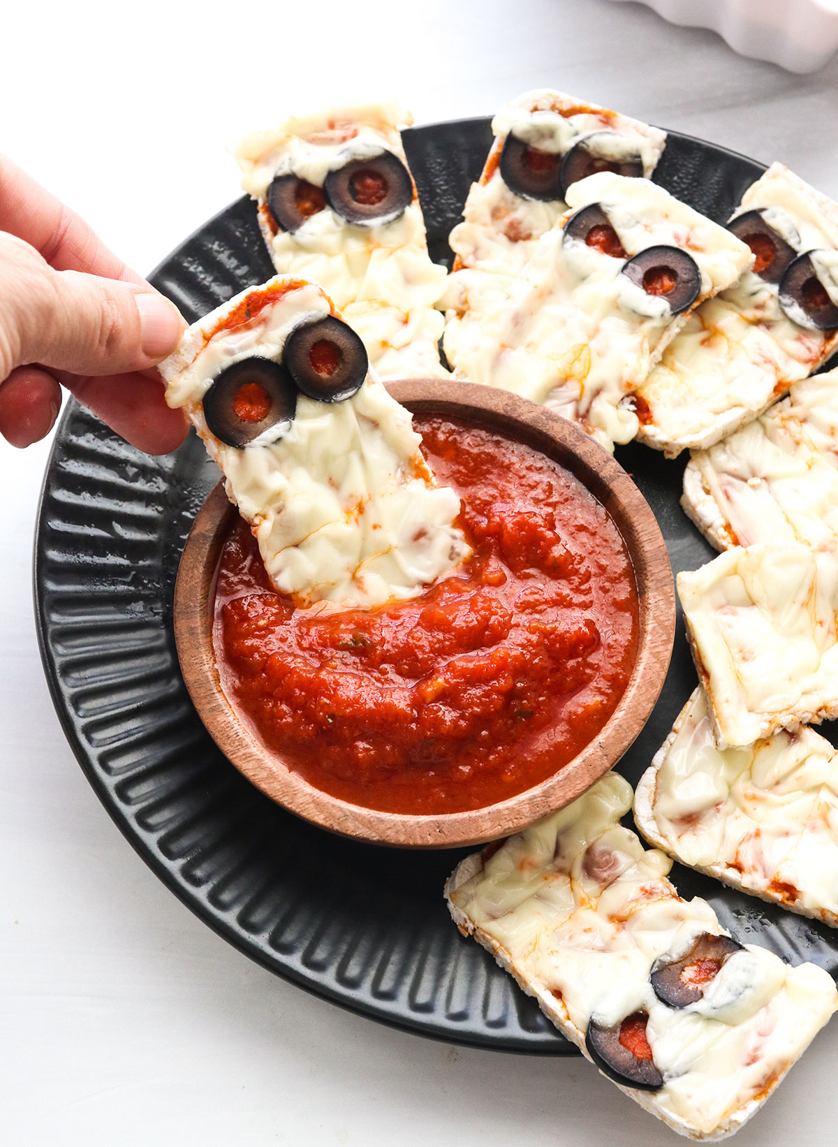 A mummy pizza dipped into a bowl of marinara sauce.