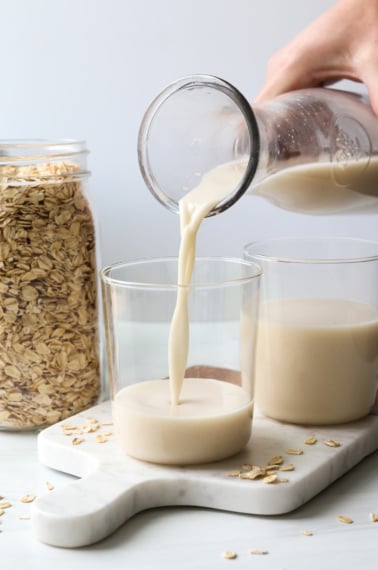 homemade oat milk poured into a glass on a marble cutting board.