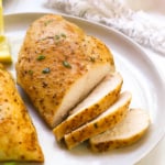 oven baked chicken breast sliced on a white plate with parsley.