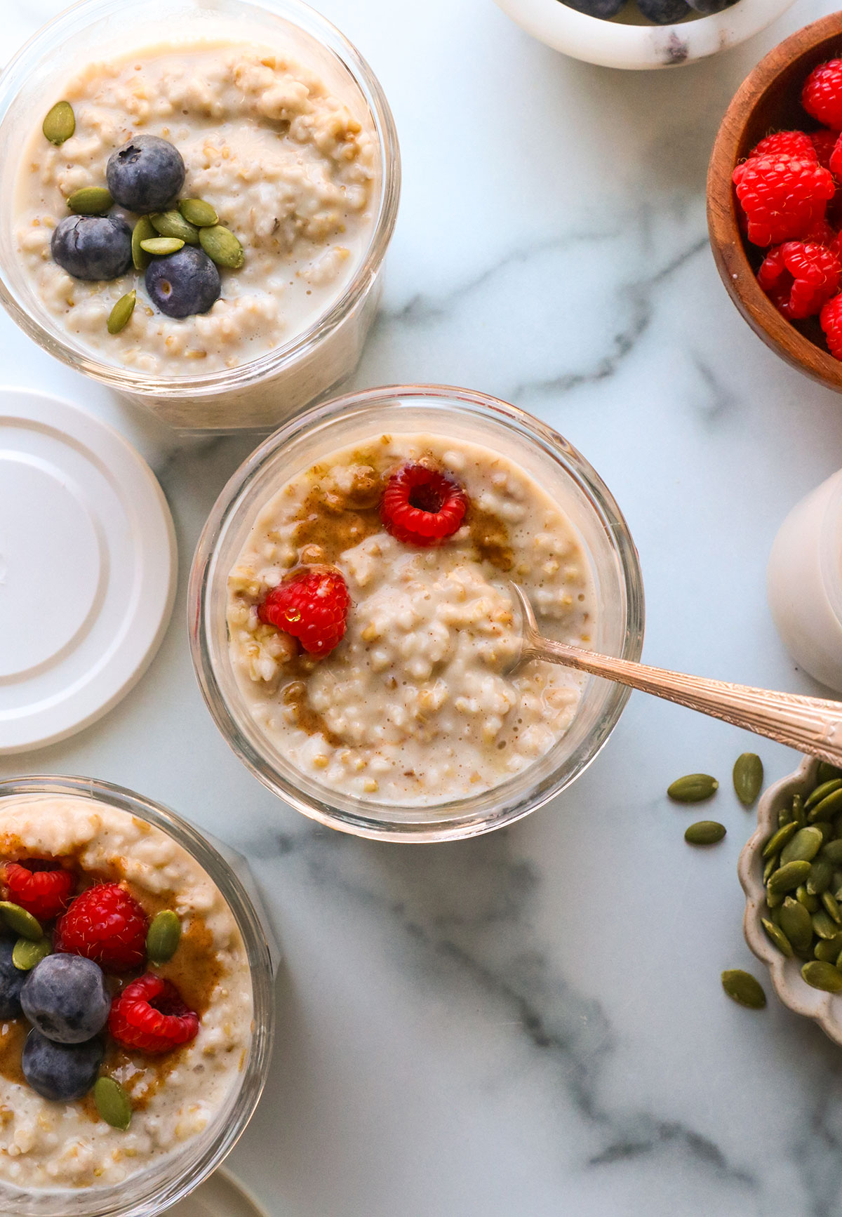 overnight steel cut oats in 3 glass jars topped with berries.