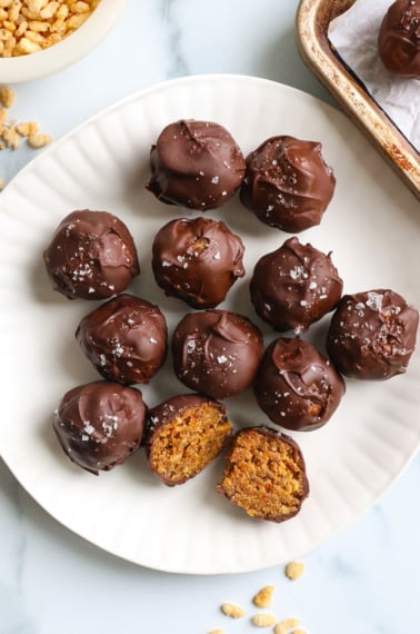 chocolate covered peanut butter balls on a white plate with one cut in half.