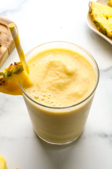 slushy pineapple smoothie in a glass with a yellow straw.