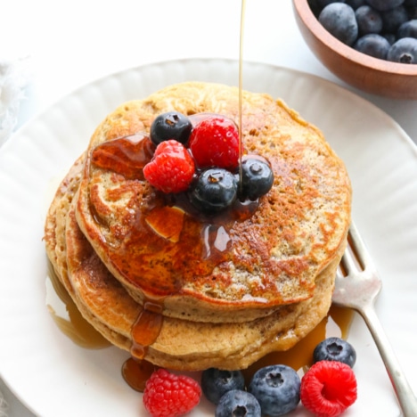 protein pancakes topped with berries and maple syrup drizzled on top.