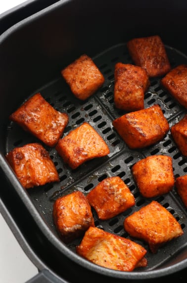 salmon bites cooked in a black air fryer basket.