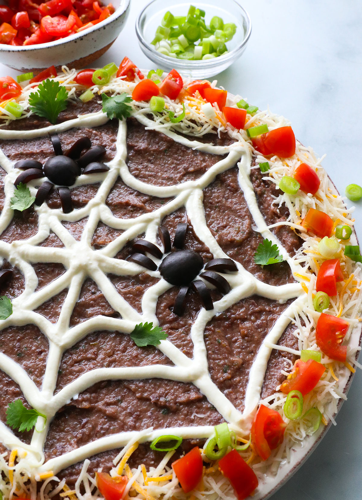 black olives added to spider web dip with chopped tomatoes and shredded cheese around the edge.