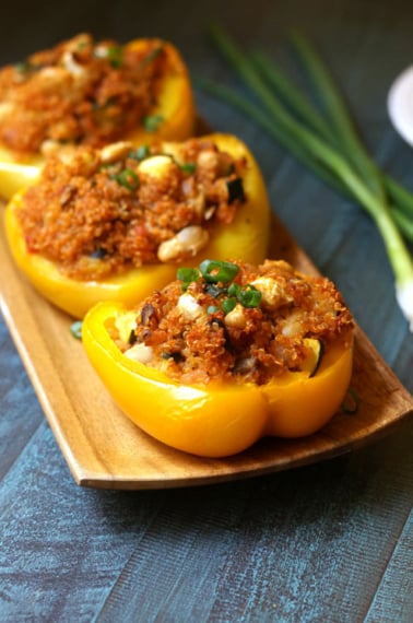 Three quinoa stuffed peppers on a wooden plate