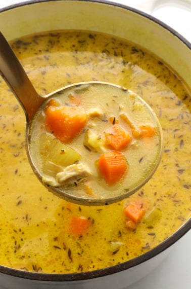 chicken turmeric soup lifted up on a ladle.