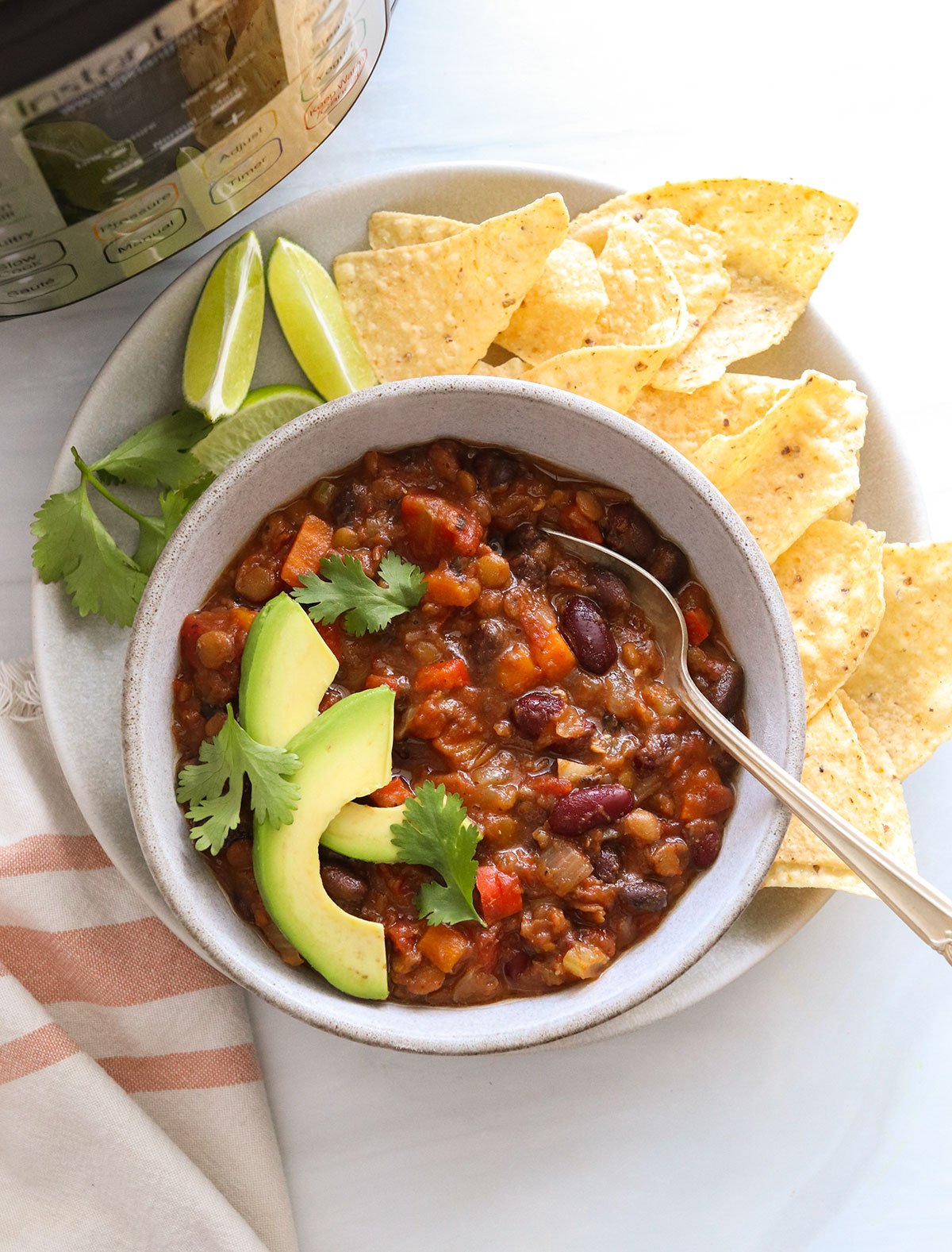 instant pot vegan chili served in a bowl with tortilla chips and sliced avocado.