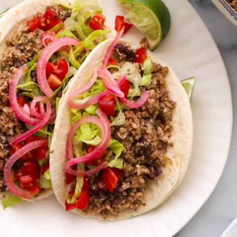 vegan tacos on a white plate with pickled red onions on top.