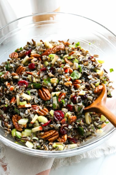 wild rice salad served in a large glass bowl with wooden spoon.